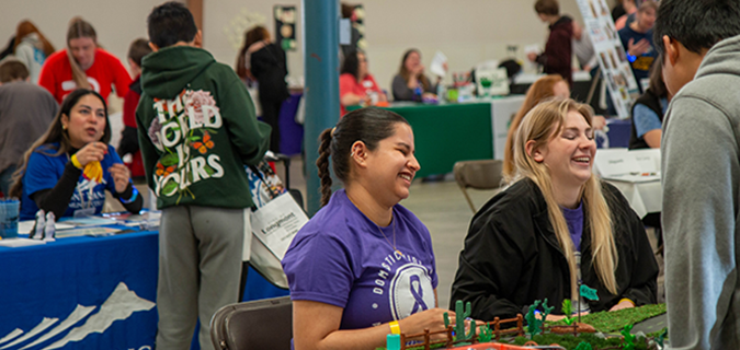 Two women are seen laughing, while seated at a table at the 2024 Youth Life Skills Fair