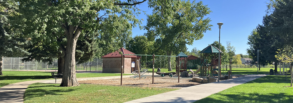 A park is seen with green grass and leafy green trees.