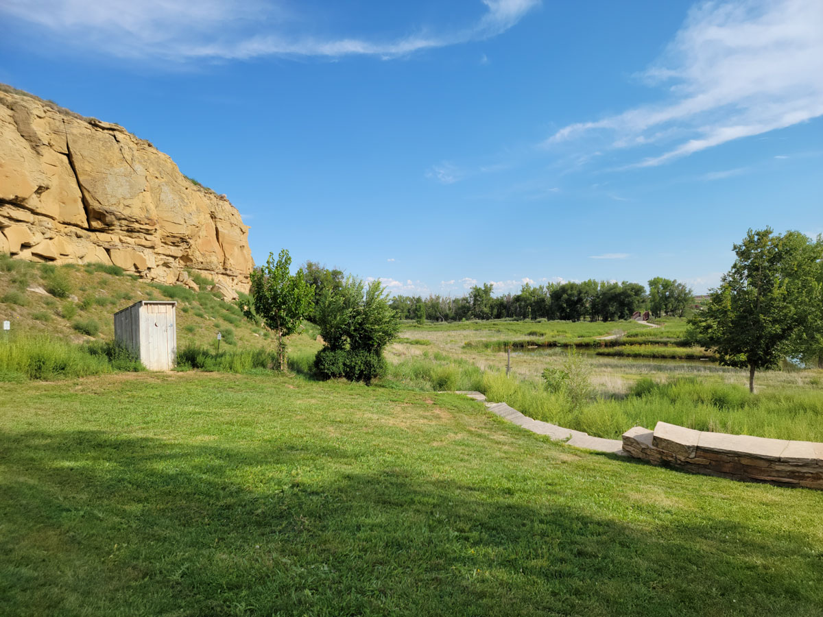 Sandstone Ranch bluffs towering above open space with grass and historic outbuildings