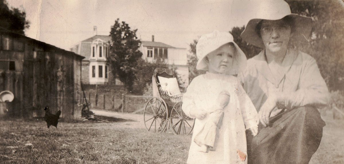 black and white historical photo of women in hat next to child in front of Sandstone Ranch house