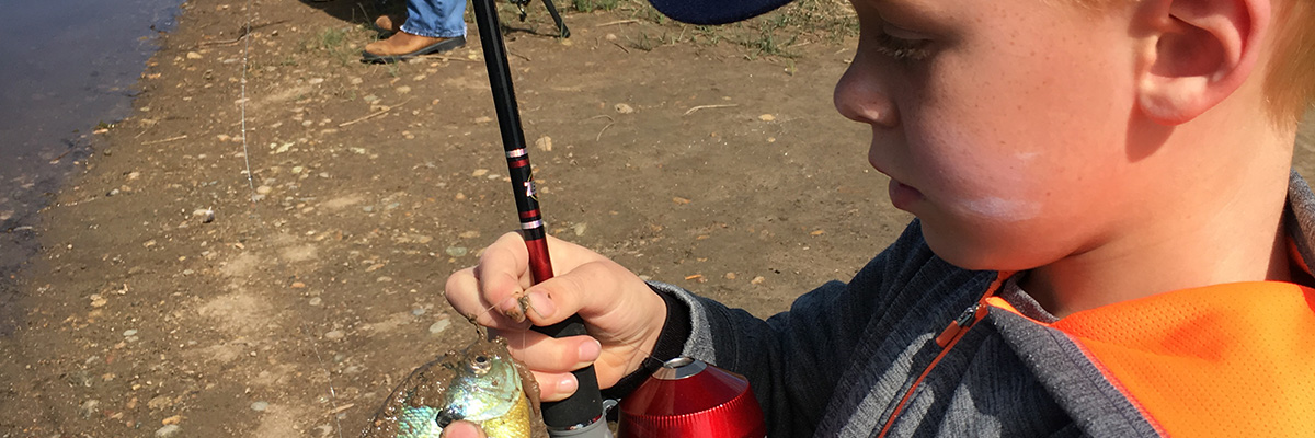 A young boy holds a fish and a fishing pole at Izaac Walton Nature Area.