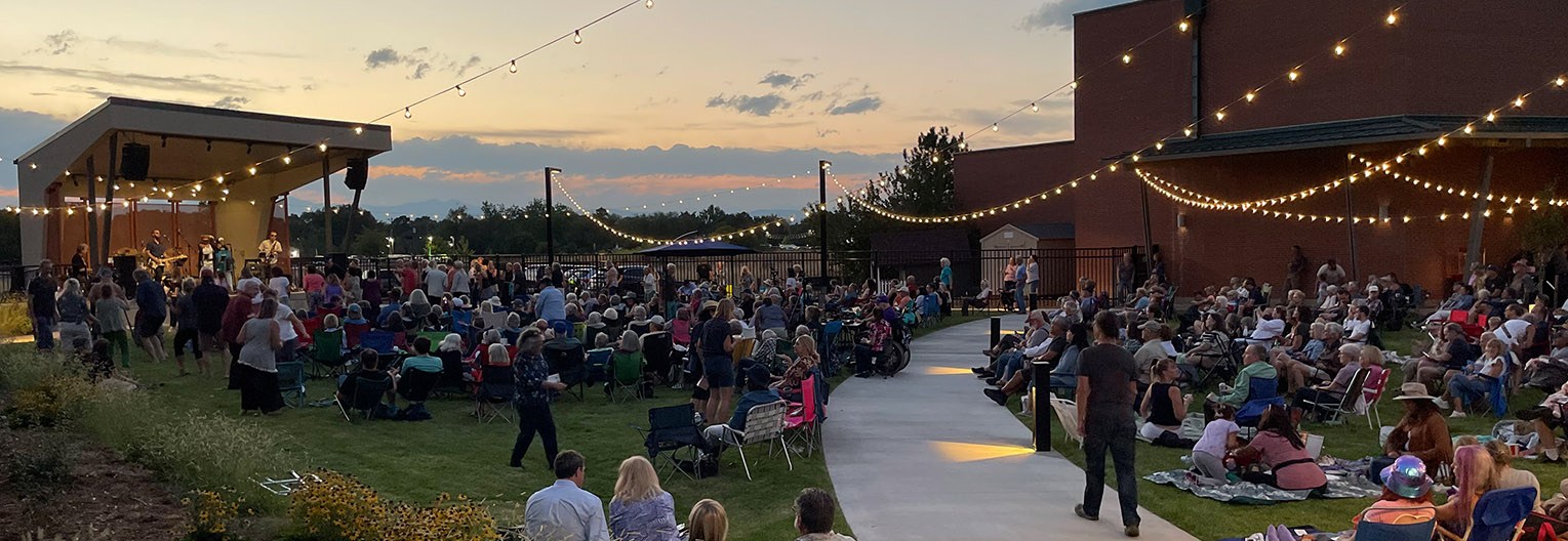 An outdoor concert at sunset with a stage and a crowd