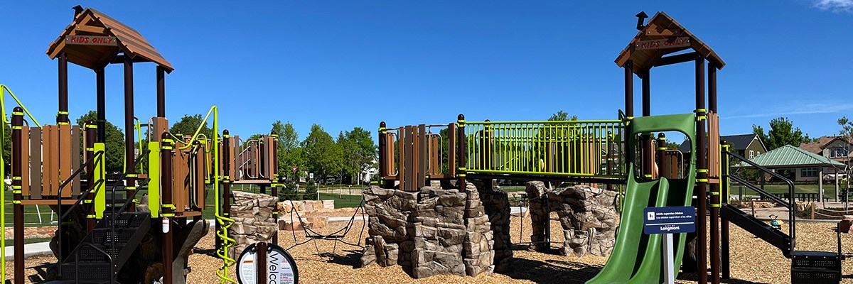 The playground at Fox Meadows Neighborhood Park is seen with tall play structures against a clear blue sky.