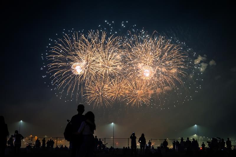 silhouettes of people watching fireworks in the background of bright flashes in the night sky