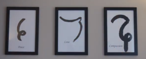 Three signs hang on the wall of Karuna Acupuncture, each with an illustration and a single word. The words, from left to right, are "Peace," "Love," and "Compassion." 