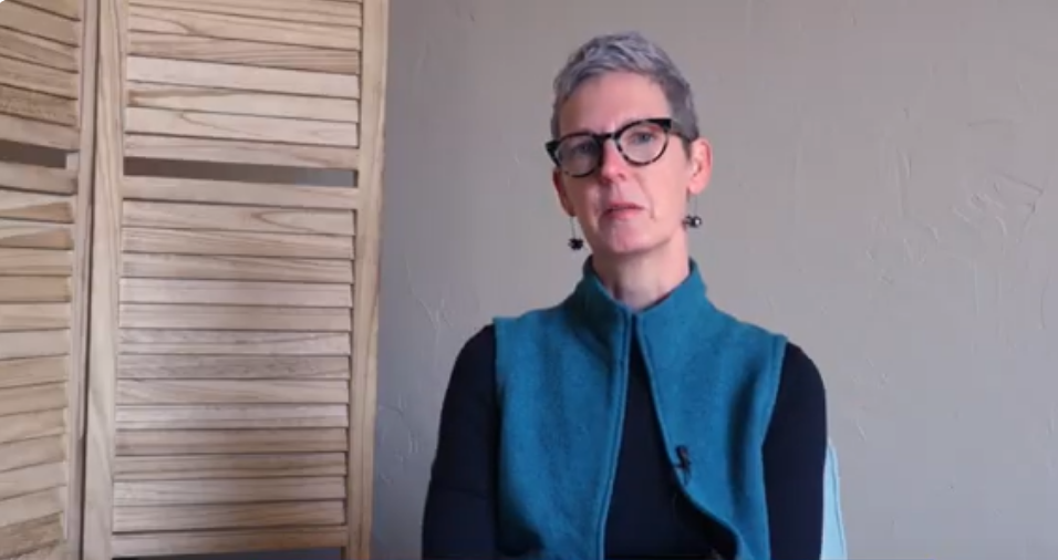 Karen Lang faces the camera with a shuttered wooden screen to her left.