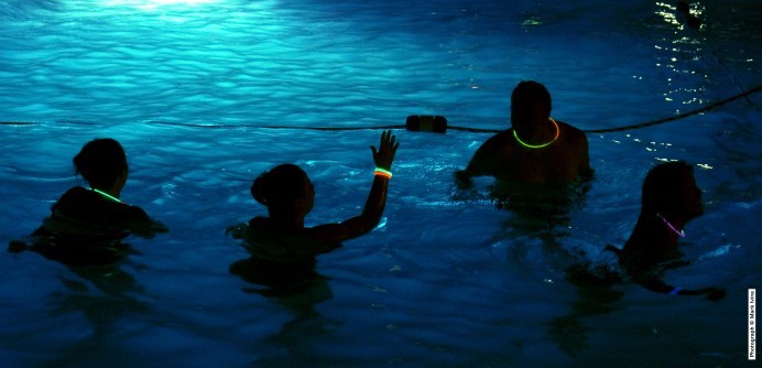 Swimmers in a pool at night with glow sticks