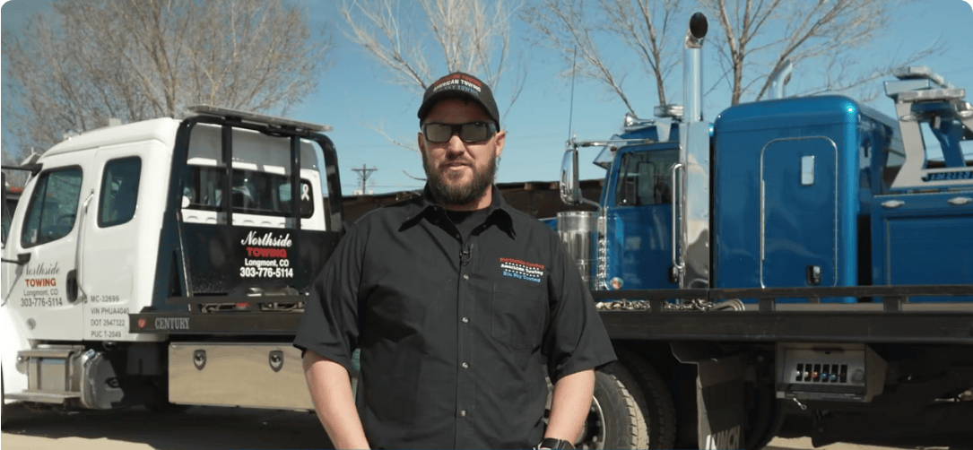 Chris Aynes of Northside Towing stands in front of one of his tow trucks, speaking.