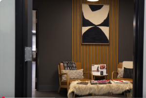 Waiting area for Rocky Mountain Beauty Bar with two chairs, a long coffee table with a furry cover and magazines, a smaller end table between the chairs with information, and an abstract painting on the wall in black and white.