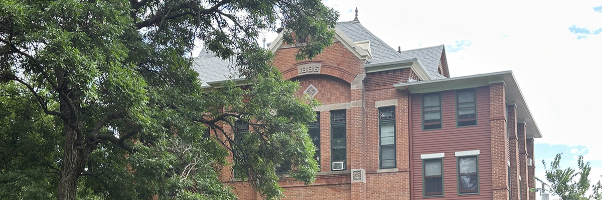The top of one of Longmont's historic brick buildings is seen surrounded by green trees.