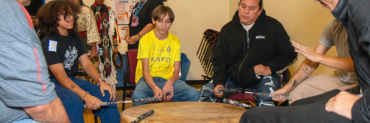 Several people are playing a drum at a Native American Heritage Month celebration