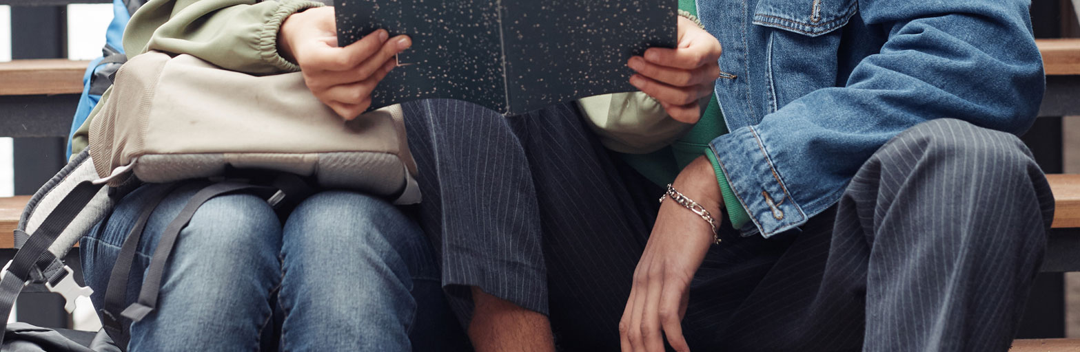close up of a couple in jeans sitting next to each other with a notebook and a purse, backpack.
