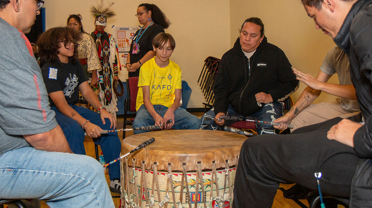 Several people are sitting around and playing a Native American drum.