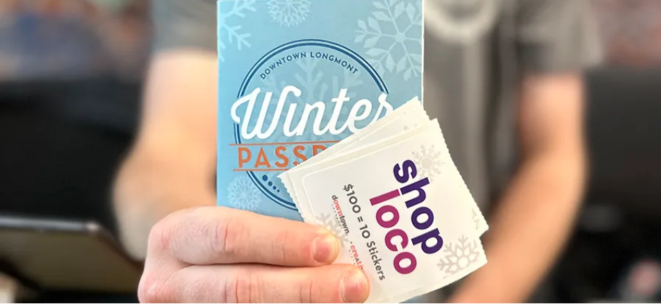 Someone is holding a Winter Passport book and some "shop loco" stickers as part of Downtown Longmont's Winter Passport program.