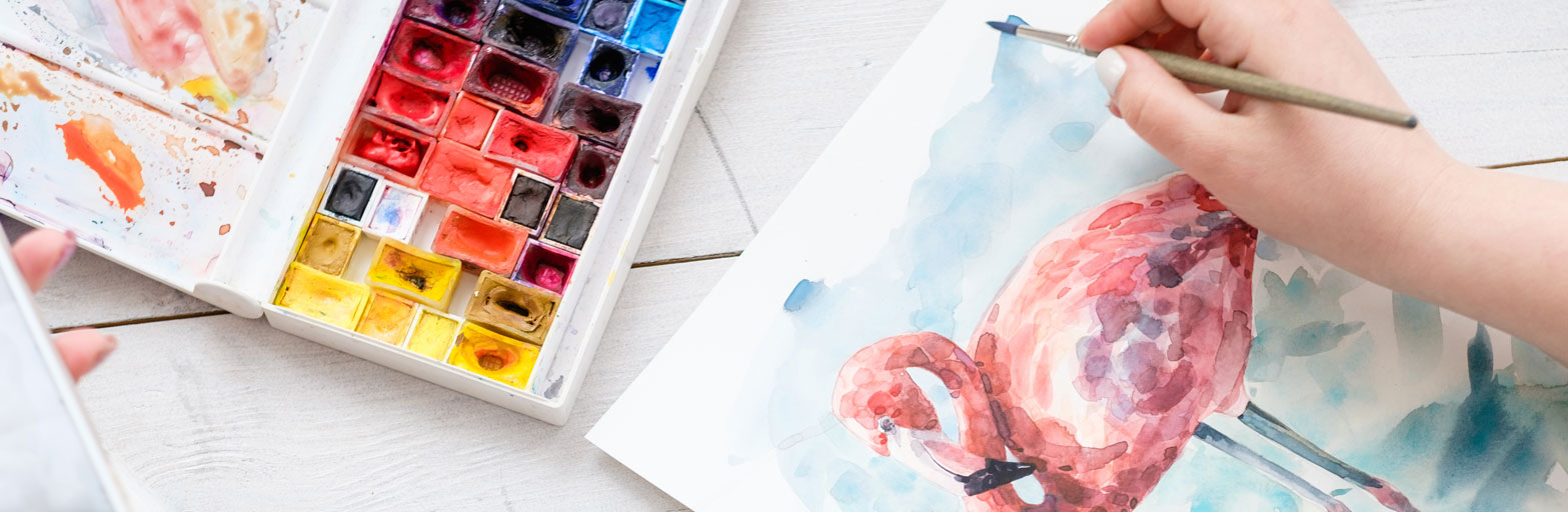 a person watercolor painting a flamingo next to a pallete of paints
