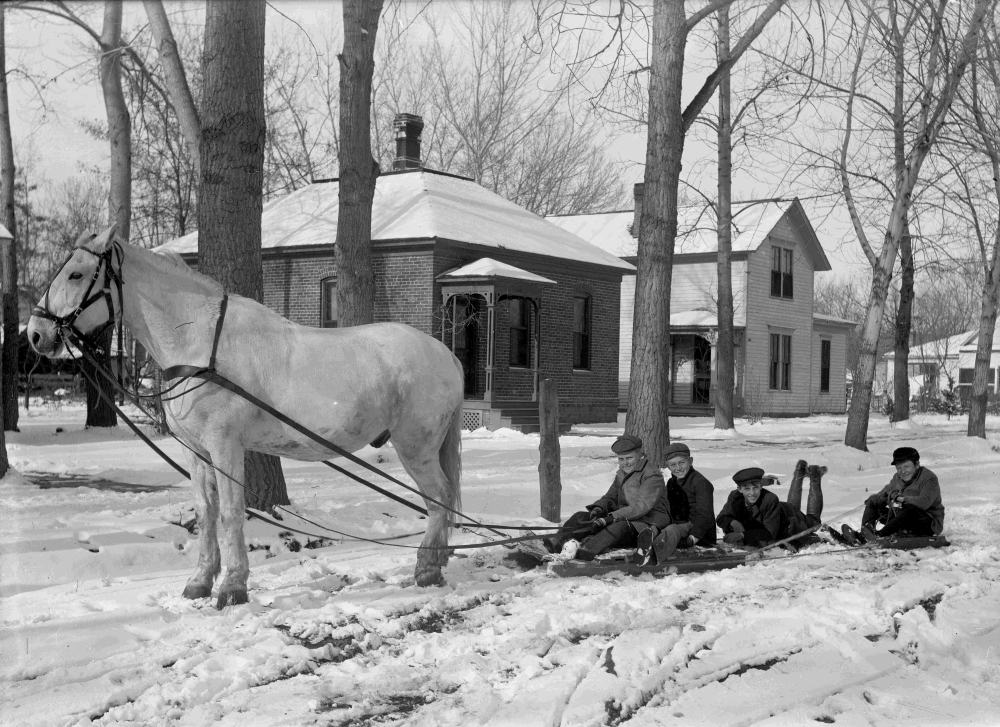 Historic black and white photo of kids on a sled pulled by a horse