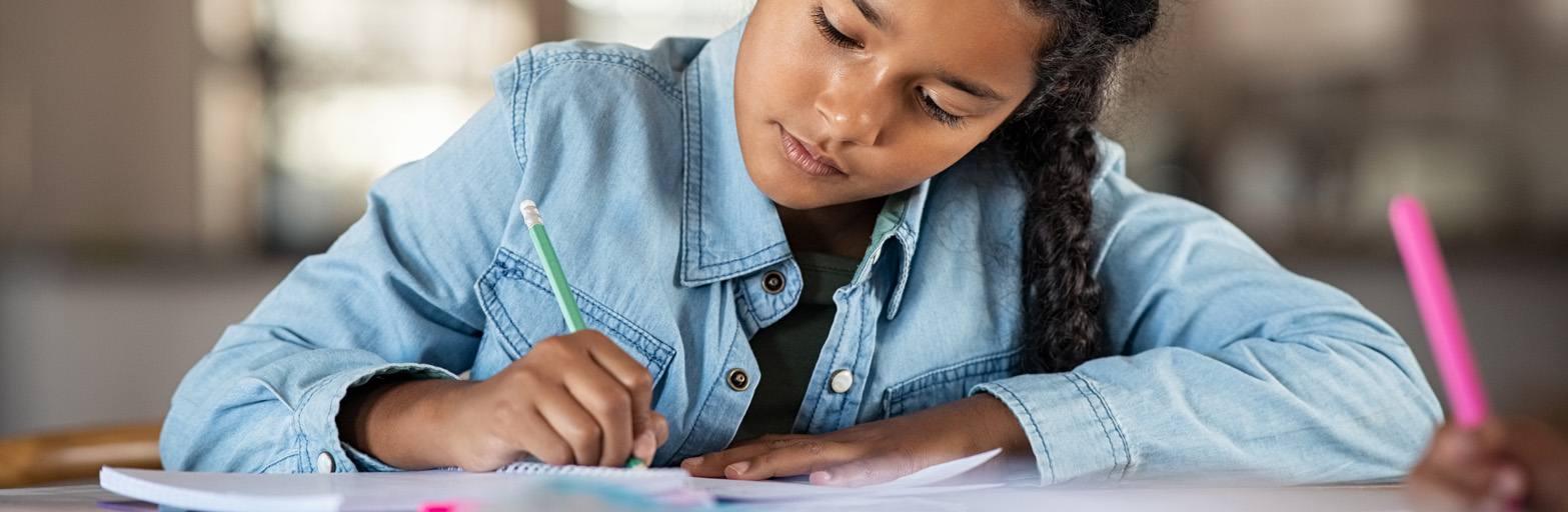 a teenage girl with black hair and a blue shirt at a desk studying with books, notebooks, and a pen.