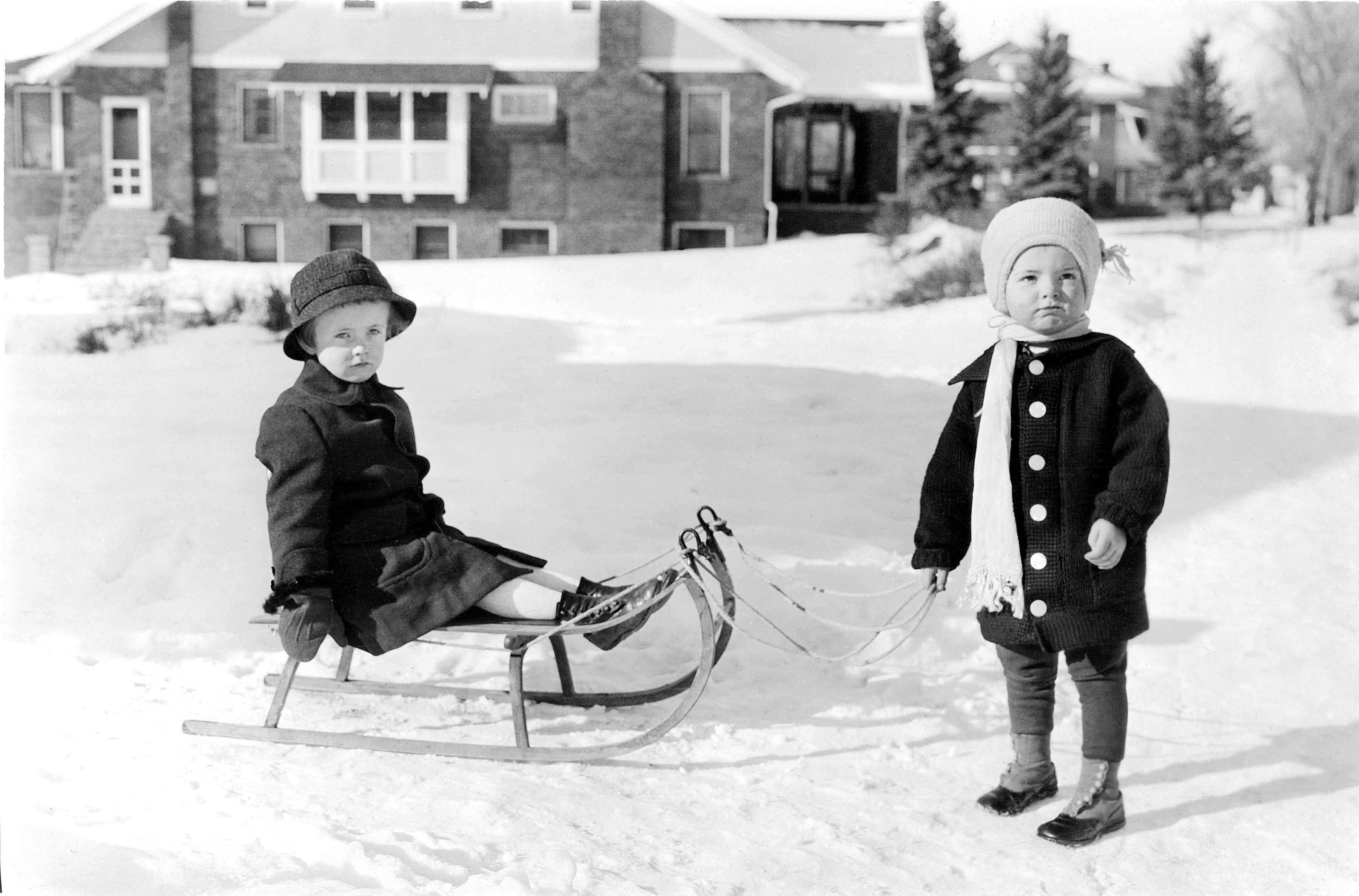 Historic black and white photo of two small children with a sled in the snow