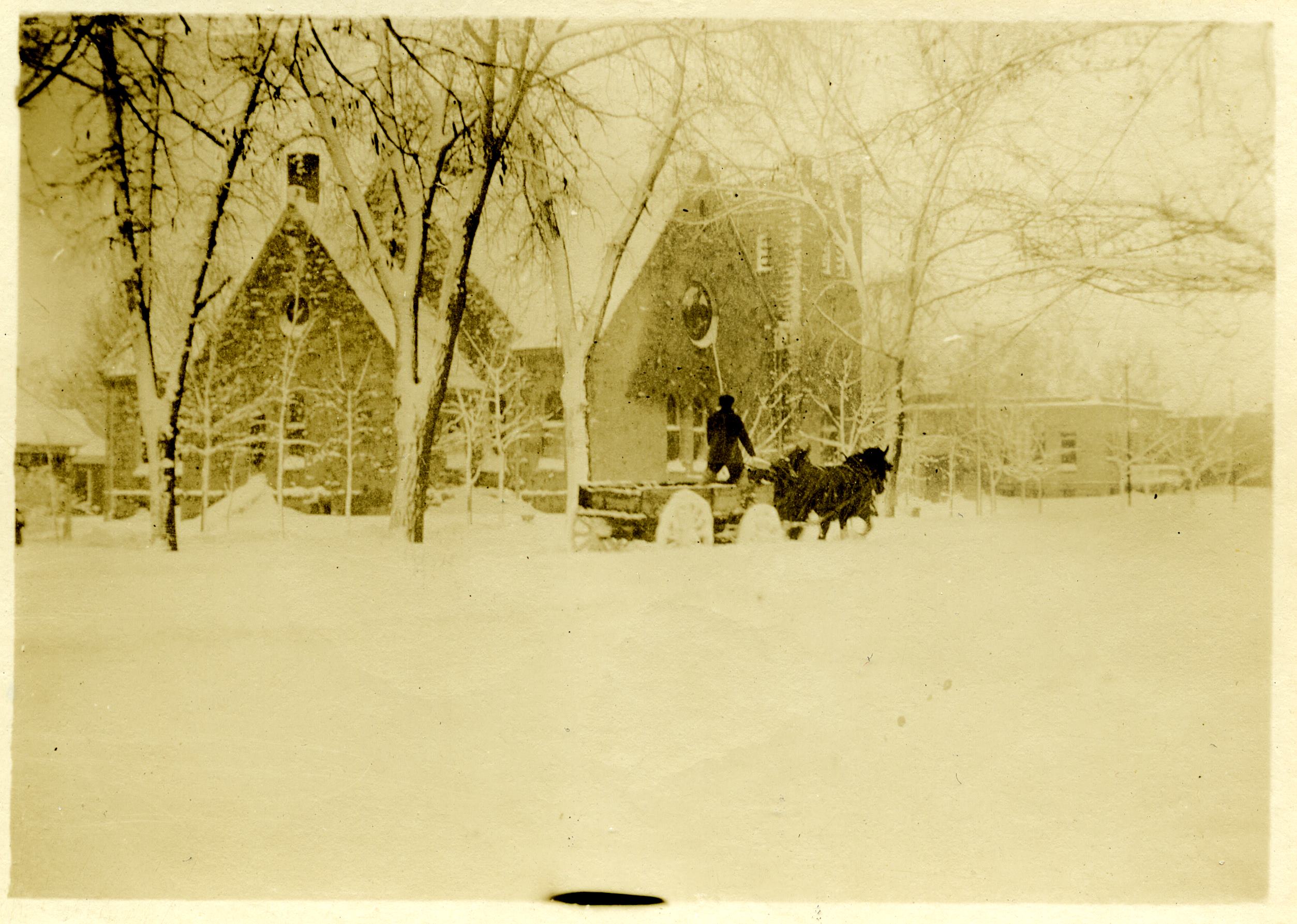 Sepia toned historic photo of a snowy street in downtown Longmont with a man on a wagon pulled by a horse