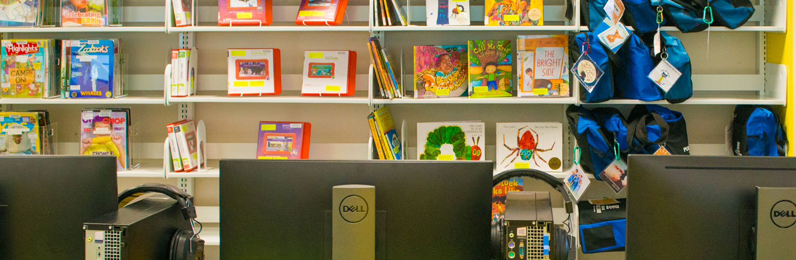 view of three backs of computer monitors in a room at the library and a desk, bookshelves and a green wall