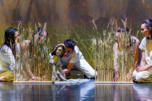 Members of Mariposa Collective guide puppet through grass props on stage.