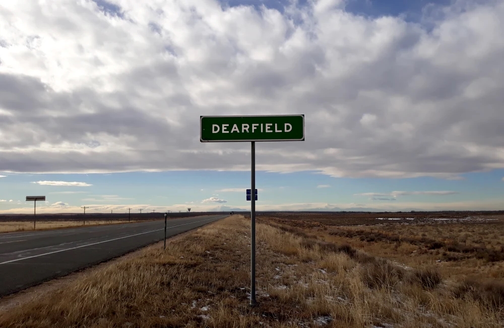 Green Dearfield road sign against a landscape of land and sky.