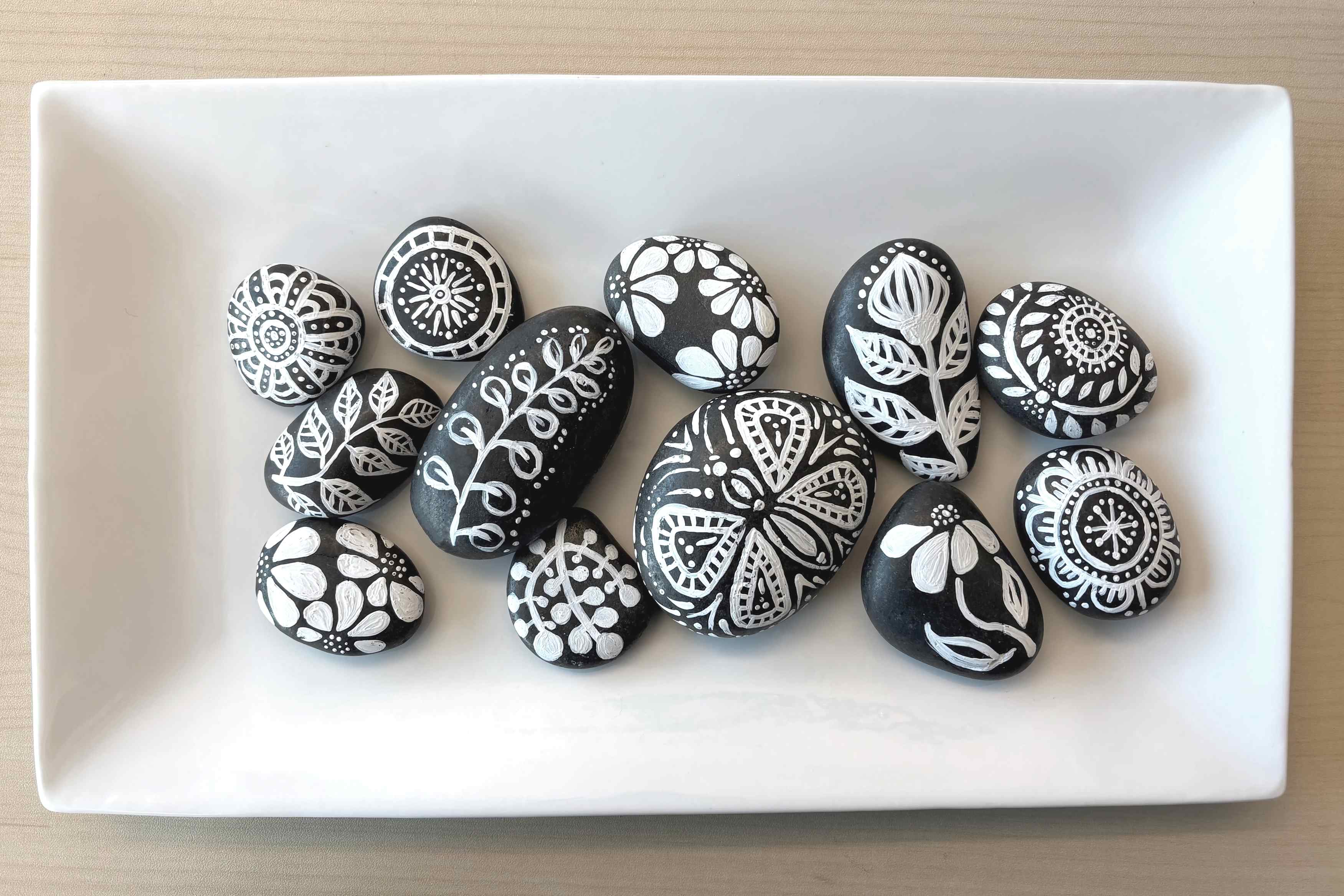 Smooth gray stones with white floral paintings on them in a variety of patterns.