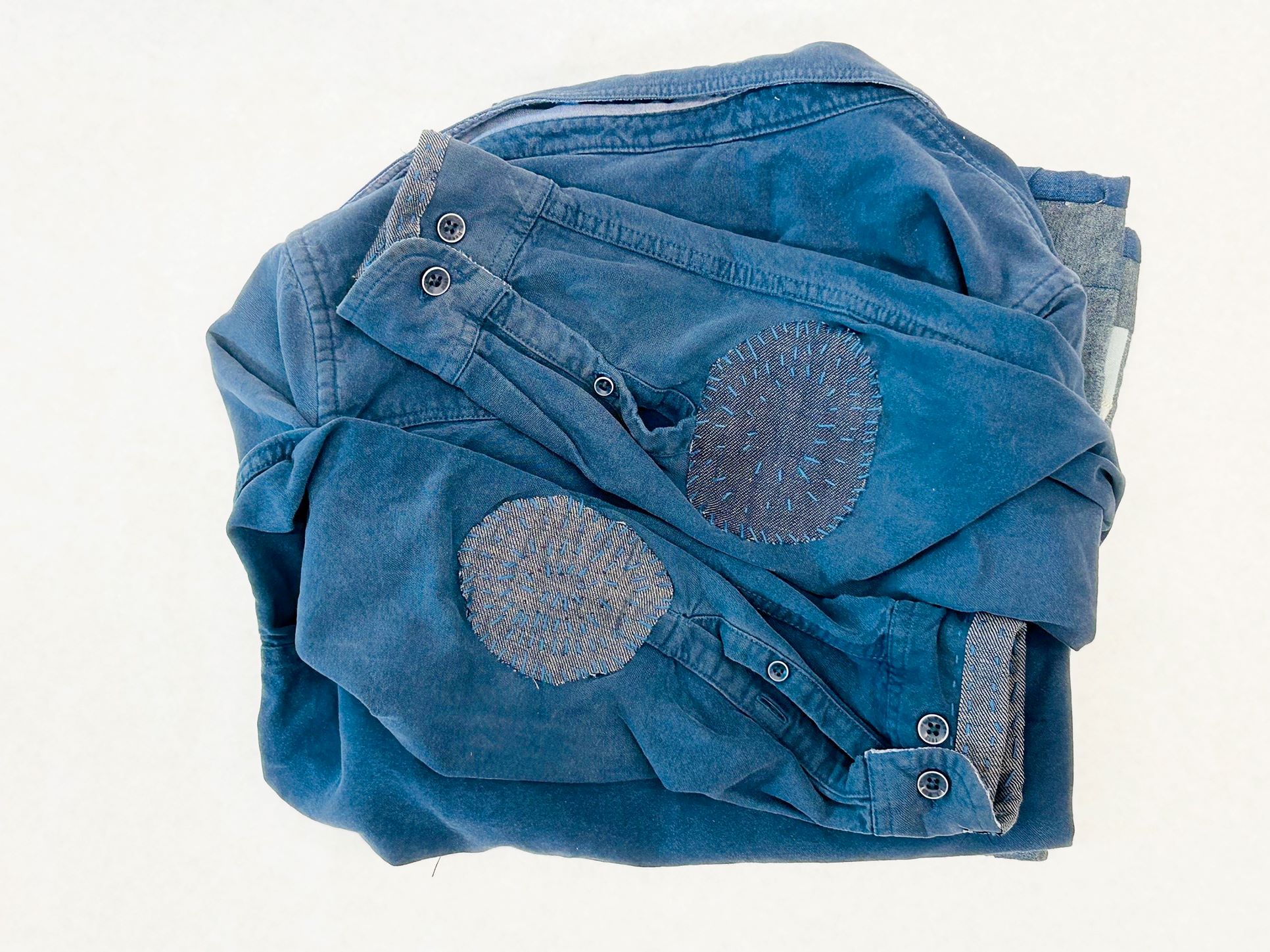 Blue jacket with visible mending (Patches and blue stitching) on the two elbows and cuffs.