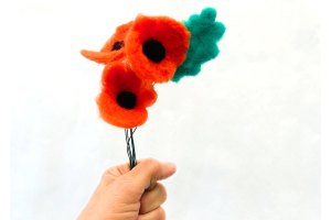 Needle felted arrangement containing three poppies (red with black center) and a green leaf attached to wire stems.