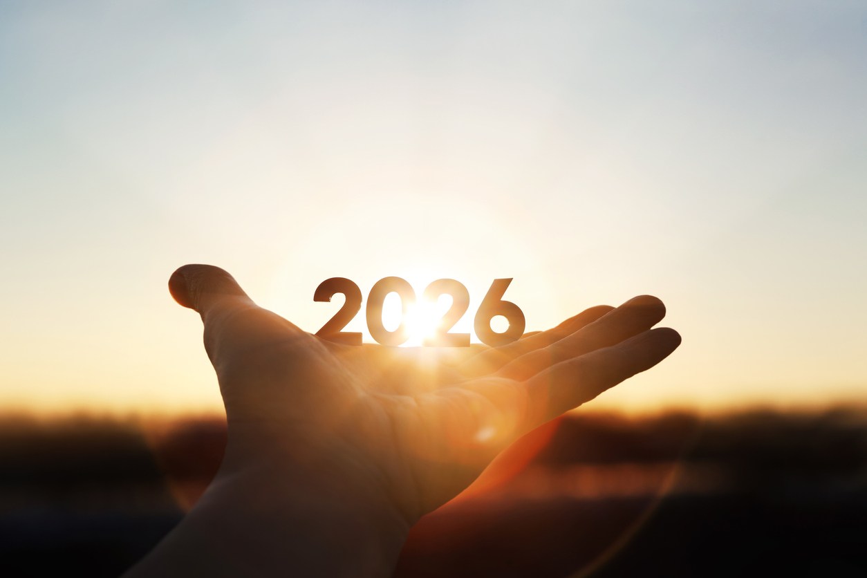 A hand holds the number 2026 as a bright sunrise shines through it.