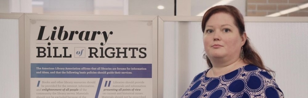 Still from The Librarians documentary that features a librarian posed next to a poster that reads "Library Bill of Rights."