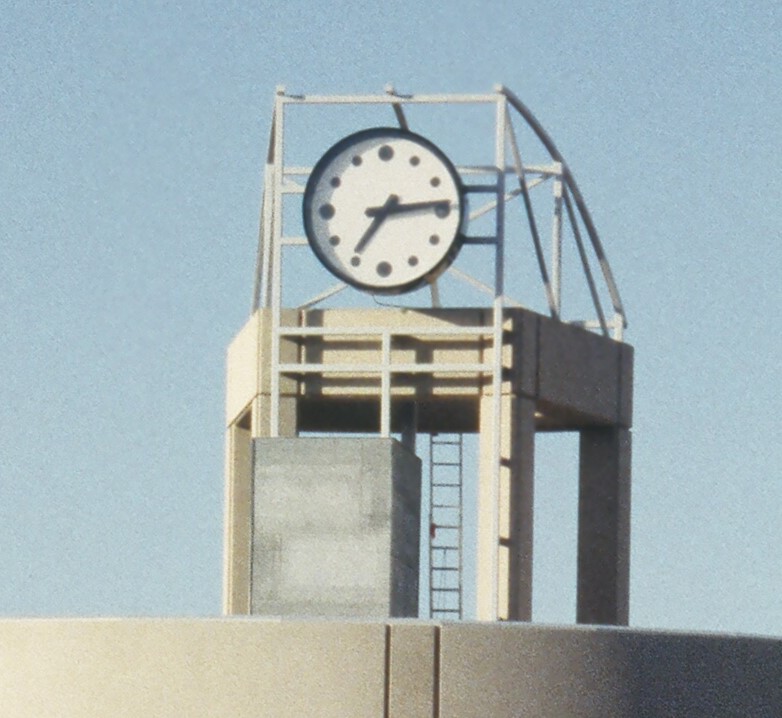 Faded image of a pale blue sky and modern clock town with concrete pillars.