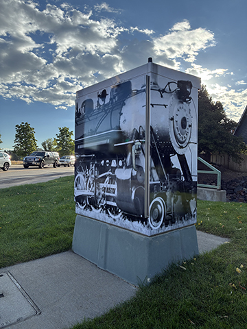 Traffic cabinet featuring an image of a train in black and white, seen from the diagonal with green grass and cloudy blue sky in the background.