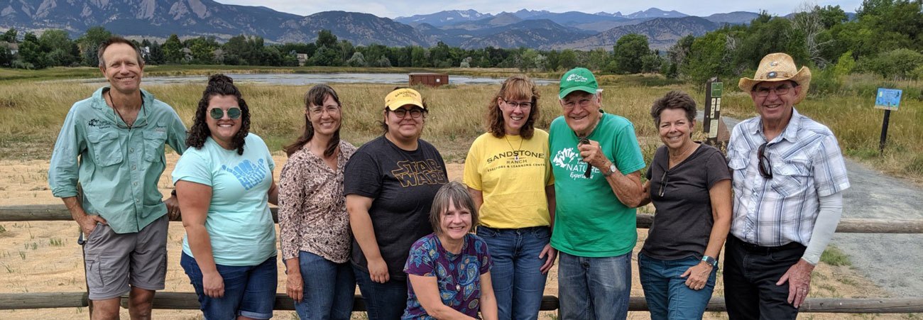 Group of Sandstone Ranch volunteers looking at camera in front of fence with mountains in the background
