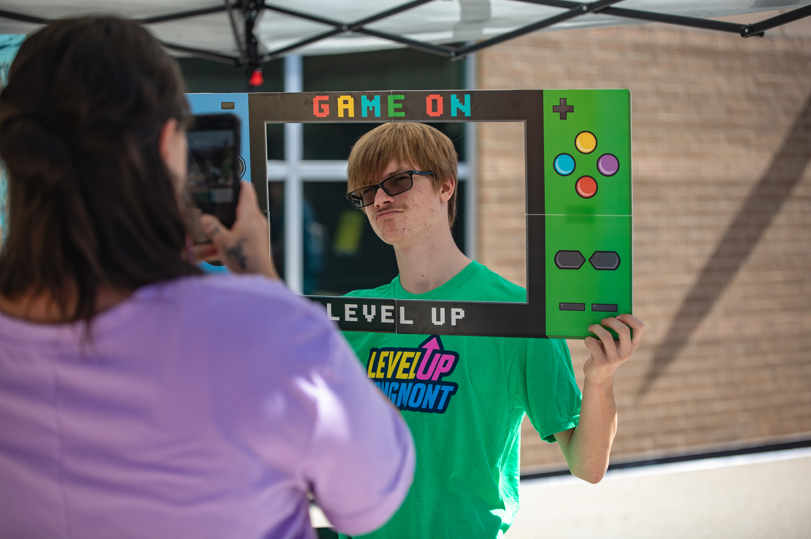 boy in green shirt looking through a photo booth hand held poster that says "Game On"