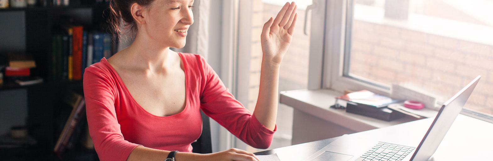 a woma n in a red shirt at a laptop engaging with her hand up.