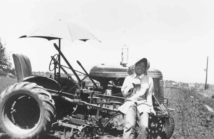 Smiling woman sitting on the front tire of a tractor