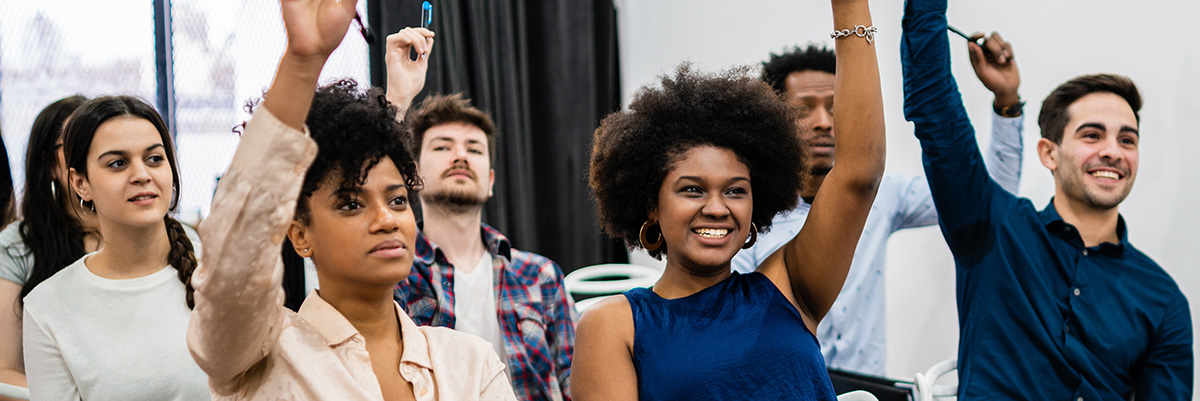 Several adults are raising their hands while seated in a classroom.