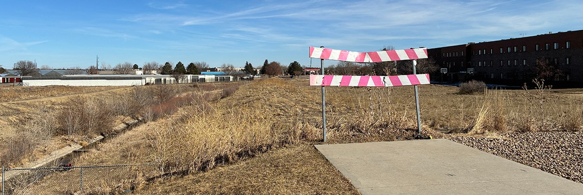 This photo show the end of a concrete trail where the future dry creek park trail will be built. There is currently a sign indicating the trail's end.