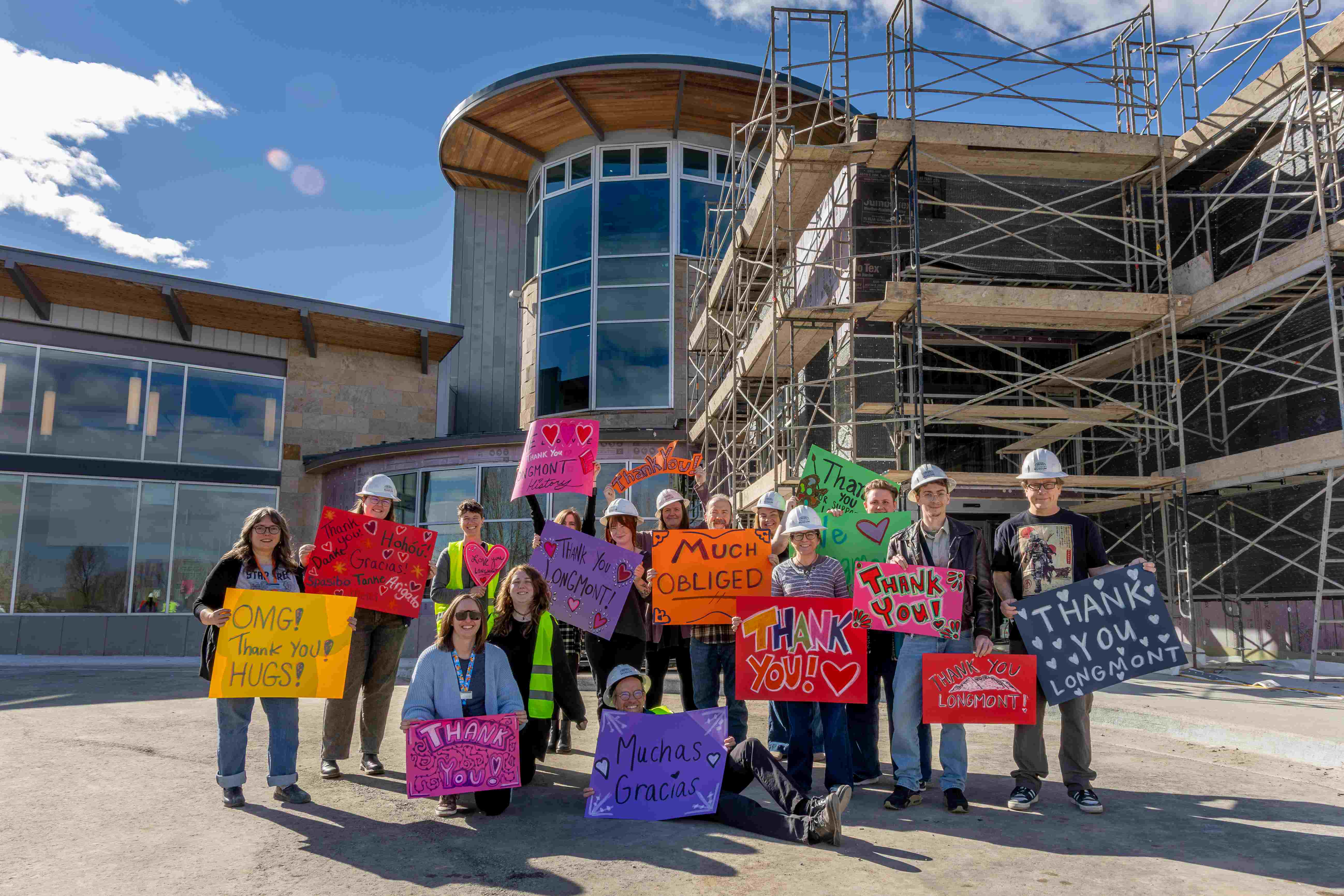 A group of people standing in front of a building under constructions holding signs of thanks