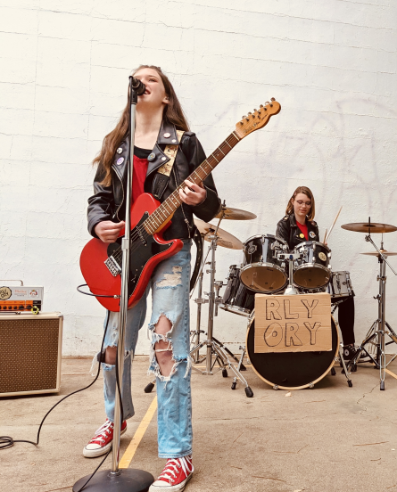 A band picture featuring a young girl playing electric guitar and singing.