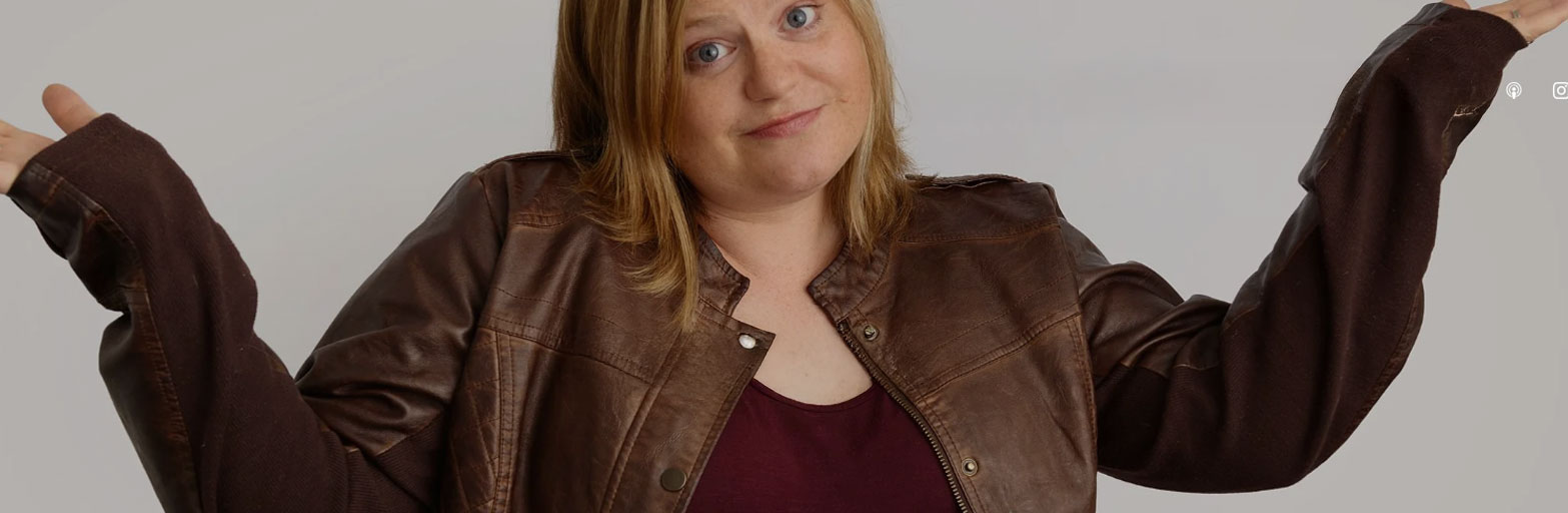 red headed woman wearing a brown leather jacket shrigging her shoulders wiht a smile on her face
