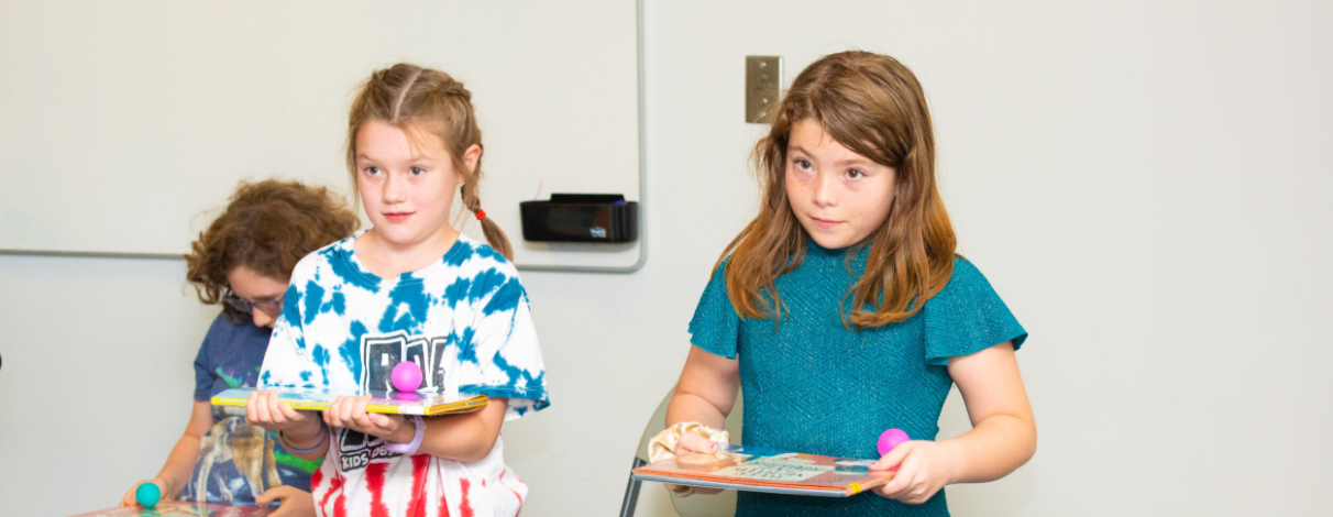 tweens playing a game indoors balancing items on a book.