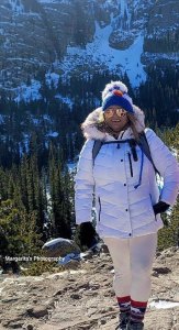 Photo of a woman wearing a winter jacket and hat posing in front of trees and snow.