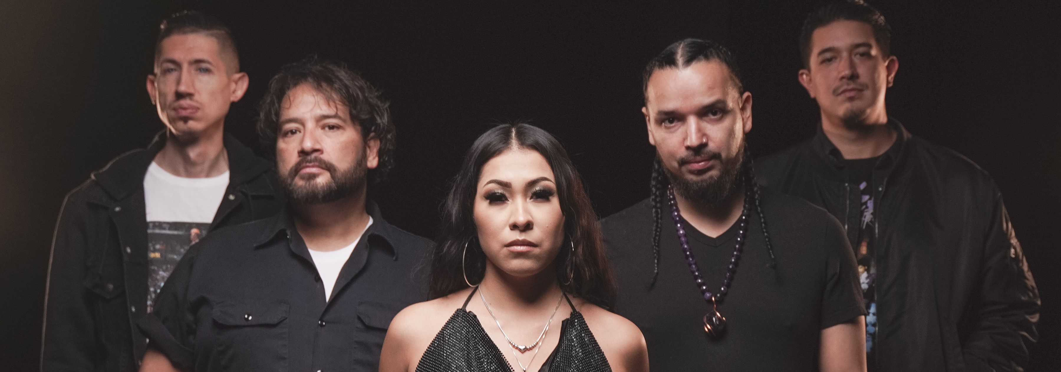 Members of 2MX2 pose together wearing a mix of black and white clothes against a black background.