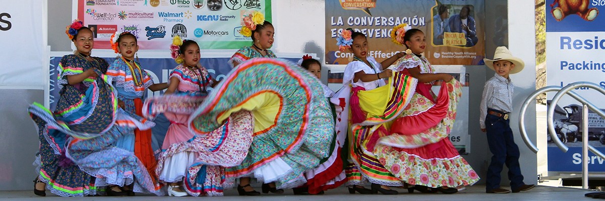 Several young girls, and one boy, dance in festive costumes at Longmont's Cinco de Mayor celebration.