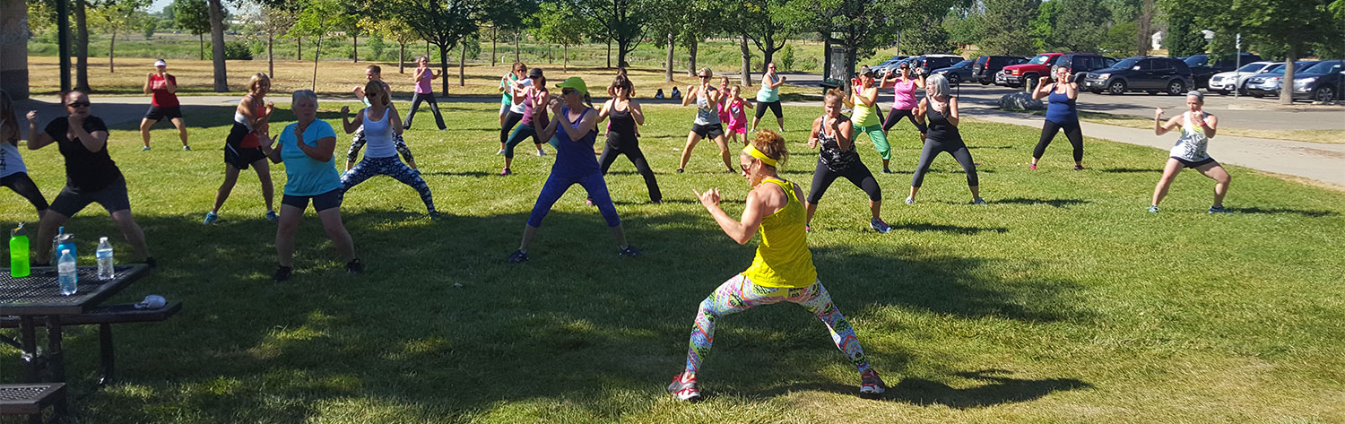 Group of people in park on grass at an outdoor fitness class with trees in the background