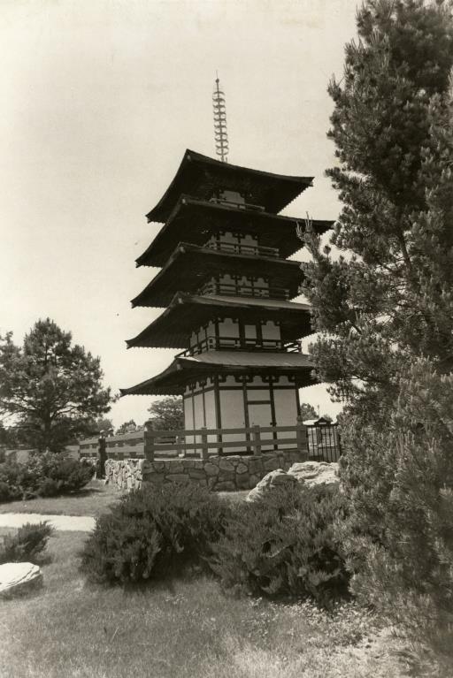 Black and white photo of the Tower of Compassion at Kanemoto Park in Longmont. Photograph shows two evergreen trees framing the tower, a five-level pagoda structure.