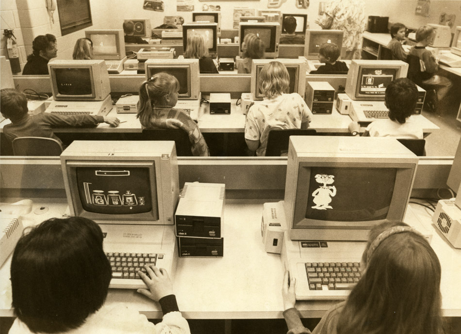 Students enjoy computer class at Loma Linda Elementary School in 1992. The photo shows four rows of students behind large white computers with large keyboards and disc drives.