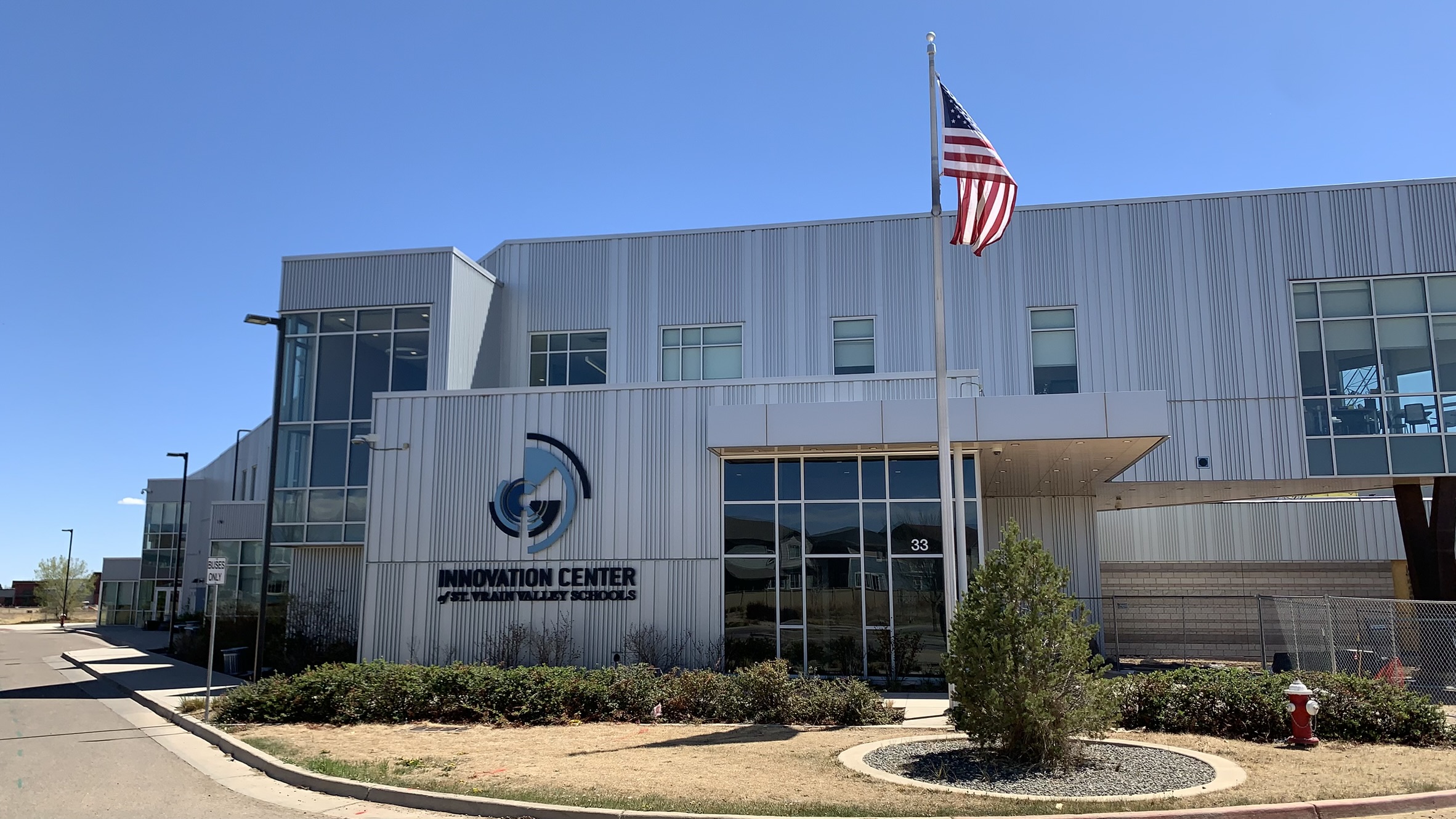 A large silver building with modern angles, the words "Innovation Center Saint Vrain Valley School Schools" on the front and a flagpole with the American flag flying.